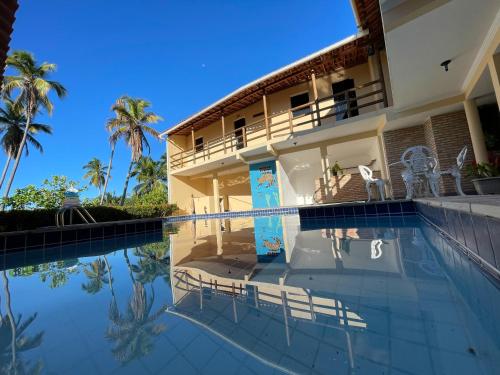 a swimming pool in front of a house with palm trees at Pousada Lua Cheia in Japaratinga
