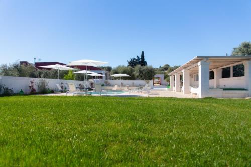 a yard with green grass and a building with umbrellas at Tenuta Amostuni-Country House in Ostuni