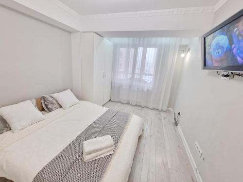 a white bedroom with a large bed and a flat screen tv at Gio Apartment in Chişinău