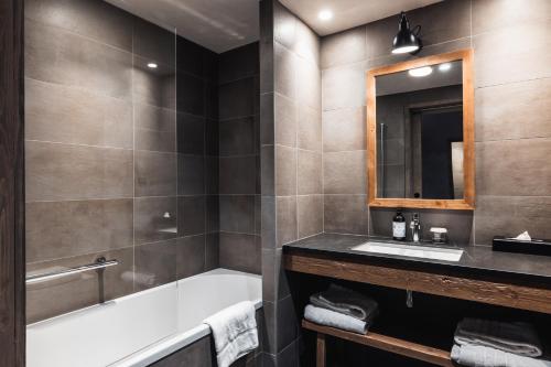 a bathroom with a tub and a sink and a mirror at Hôtel de la Roche in Beaufort