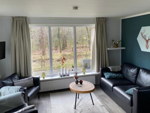 een woonkamer met een bank, een tafel en een raam bij Chalet de Bosrand 404, unieke rustige plek met veel privacy aan de bosrand van vakantiepark op de Veluwe in Beekbergen