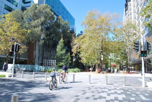 two people riding bikes down a street in a city at The Sebel Canberra Civic in Canberra