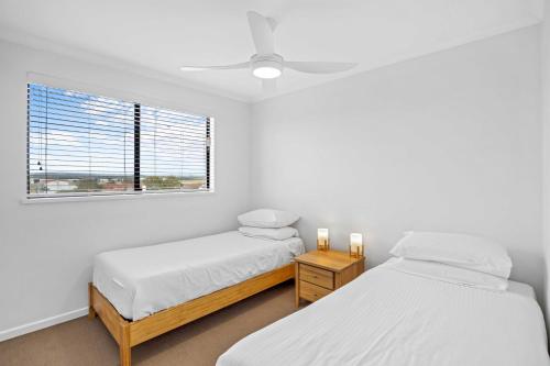 two beds in a white room with a window at Beachside 3-Bed with BBQ, Pool, Gym & Tennis Court in Marcoola