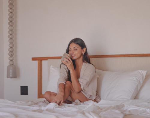 a woman sitting on a bed drinking from a cup at Ukiyo San Agustinillo in San Agustinillo
