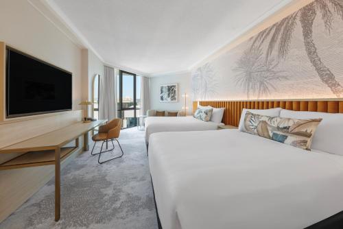 a hotel room with two beds and a desk at Amora Hotel Brisbane in Brisbane