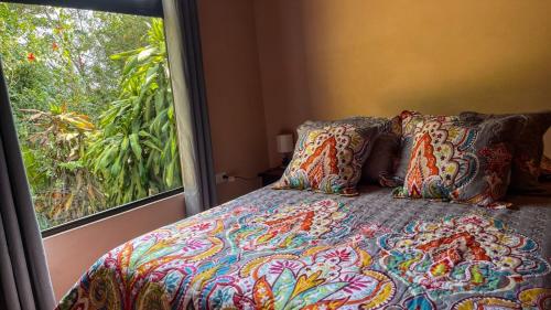 a bed with a colorful comforter and pillows next to a window at Casa Euphonia Monteverde in Monteverde Costa Rica