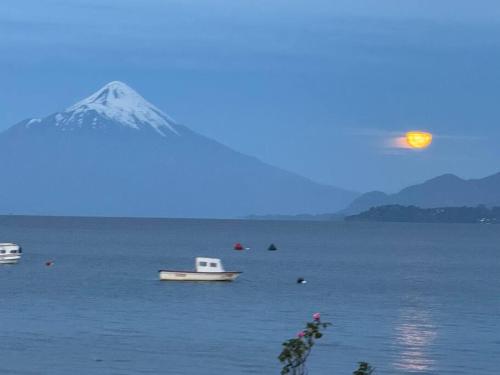 a mountain and a boat in the water with a moon at Depa con piscina frente al Lago Llanquihue y vista al volcán in Puerto Varas
