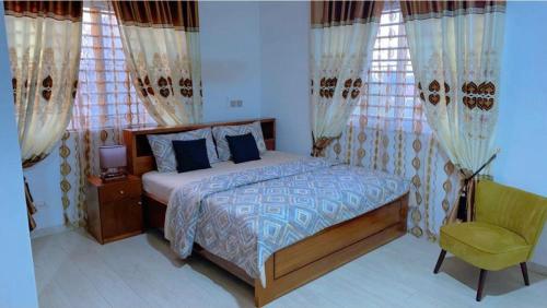 a bedroom with a bed and a chair and windows at Ayan Villas in Accra