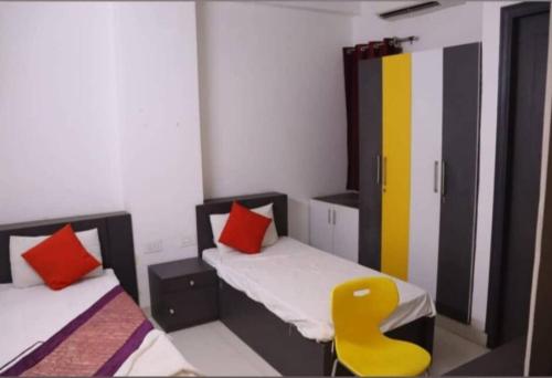 Cette chambre comprend 2 lits et une chaise jaune. dans l'établissement Ashiyana Homes, à New Delhi