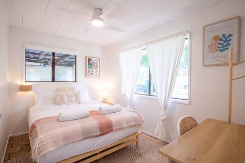 a white bedroom with a bed and a table at Cosy Straddie cottage + sleeps 6 + close to beach in Point Lookout