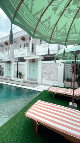 勒吉安的住宿－Kaktus Boutique Apartments Bali - ADULTS RETREAT，一个带两把躺椅的绿色遮阳伞下的游泳池