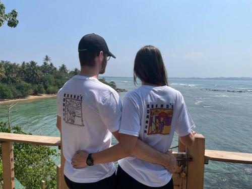 a man and woman standing on a balcony looking at the ocean at Kenno's Korner in Weligama