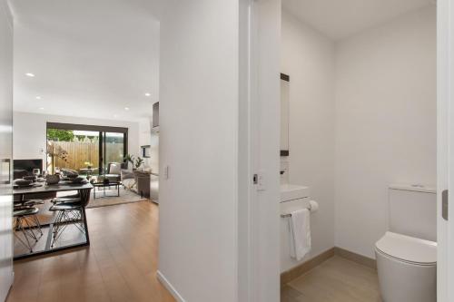 a white bathroom with a toilet and a kitchen at Stylish New 8 Mins CBD Free Parking in Christchurch