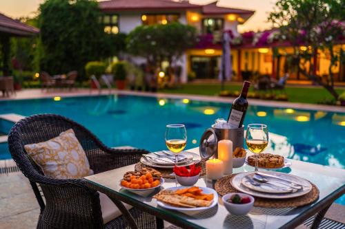 a table with food and wine next to a pool at StayVista at Moksh Villa - BBQ & Jacuzzi in Alibaug