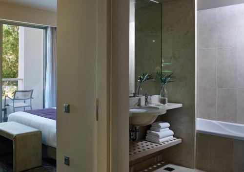 a bathroom with a sink and a mirror and a bed at Atlantica Akti Zeus Hotel in Amoudara Herakliou