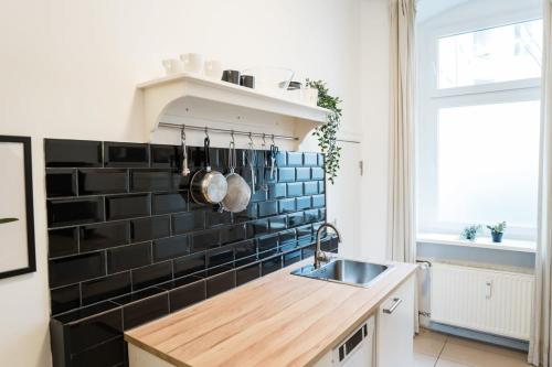 Great Apartment for Eight in Berlin Neukölln في برلين: مطبخ مع حوض وجدار من البلاط الأسود
