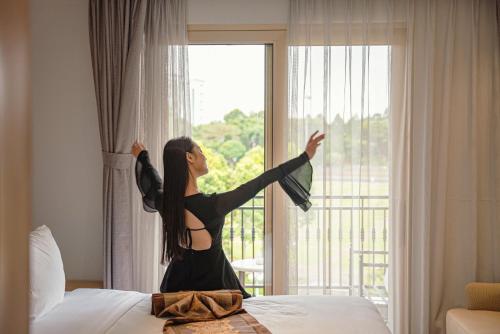 a woman is standing on a bed looking out a window at Ngon Avatar Hotel in Pleiku