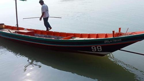 Un uomo in piedi su una barca in acqua di HomeSatay Songpeenong โฮมสเตย์สองพี่น้อง a Chumphon