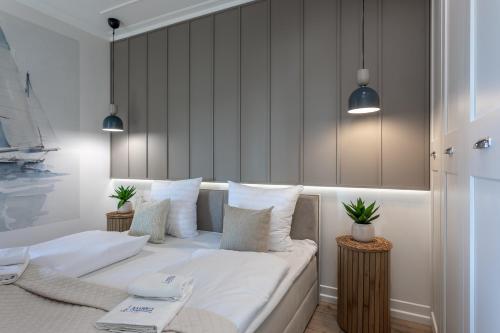 um quarto com uma cama com lençóis brancos e almofadas em Ambria Apartments Jachtowa em Świnoujście