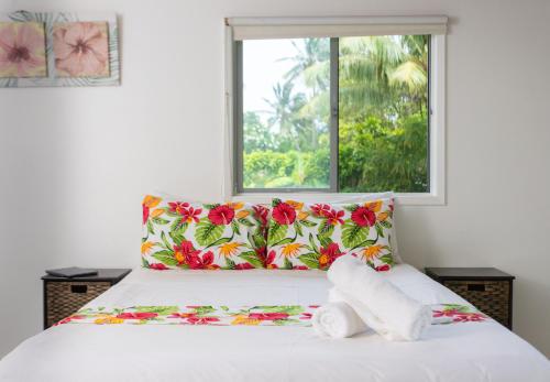 a bedroom with a bed with colorful pillows and a window at Bella Beach Bungalows in Rarotonga