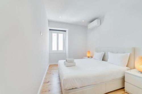 ein weißes Schlafzimmer mit einem weißen Bett und einem Fenster in der Unterkunft Cozy Coastal Getaway 3BR Apartment in Estoril in Estoril