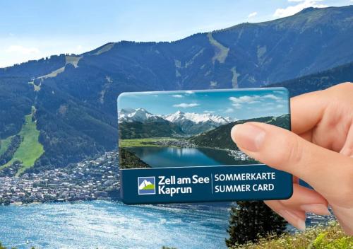 uma mão segurando um cartão com uma foto de um lago em carpe solem KAPOOM - Branded Apartments incl Zell am See-Kaprun Summer Card em Kaprun