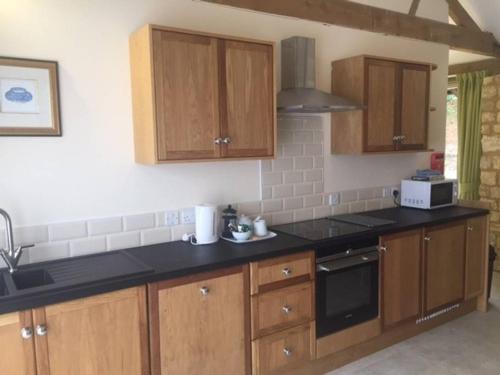 a kitchen with wooden cabinets and a black counter top at Hares Scrape at Tove Valley Cottages in Towcester