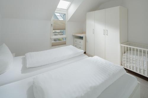 a white bedroom with a bed and a crib at Ferienhaus Haus an der Mühle in Norderney
