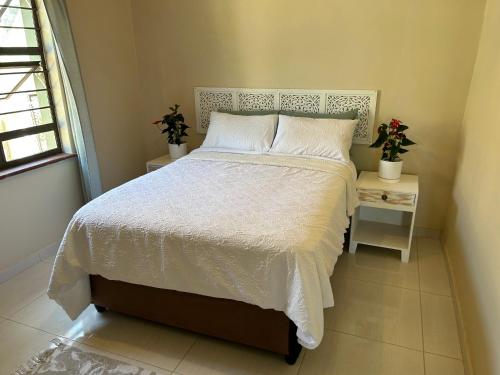 a bedroom with a white bed with two tables and a window at Ocean Village in Amanzimtoti
