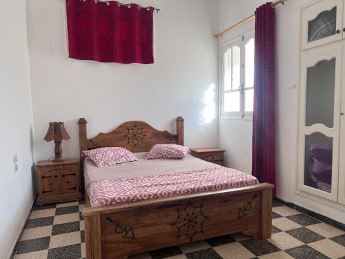 a bedroom with a wooden bed with red curtains at App s+2 RDC in Tozeur