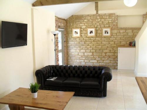 a black leather couch in a living room with a table at Otters Holt at Tove Valley Cottages in Towcester