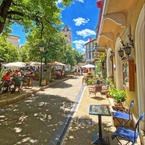 une rue avec des tables et des chaises et des personnes assises aux tables dans l'établissement Via Venaissia, à Pernes-les-Fontaines