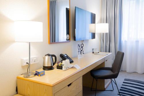 a hotel room with a desk with a lamp and a chair at Novotel Manchester West in Worsley