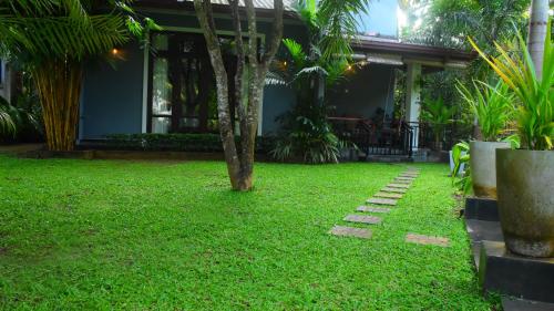 a green yard with a tree in front of a house at Leel’s Safari Cottage in Udawalawe