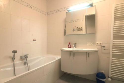 La salle de bains blanche est pourvue d'un lavabo, d'une baignoire et d'un miroir. dans l'établissement Villa Duindoorn 2.302, à Cadzand