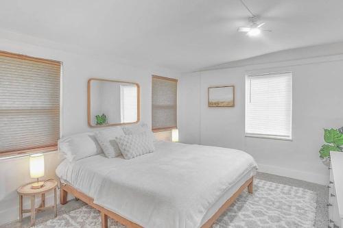 a white bedroom with a bed and two windows at Central, Cozy Retreat in Vero Beach