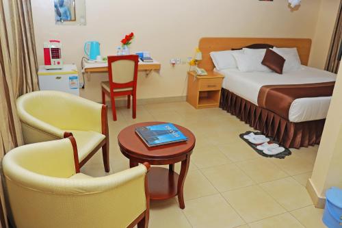 Dereva Hotel Rwamagana في Rwamagana: غرفة فندقية بسرير وطاولة وكراسي