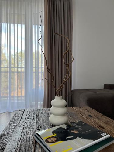 a living room with a table with a vase on it at Saulės Tako apartamentai in Druskininkai