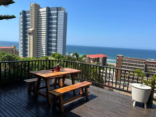 a wooden table and bench on a balcony with the ocean at Ocean Village in Amanzimtoti