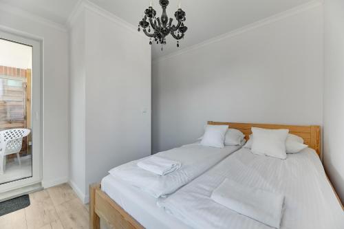 Grobla Centrum 3 by Grand Apartments في غدانسك: غرفة نوم مع سرير مع شراشف بيضاء وثريا