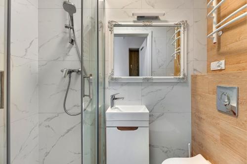a bathroom with a shower and a sink and a mirror at Grobla Centrum 3 by Grand Apartments in Gdańsk