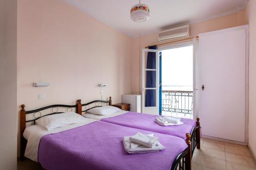 ein Schlafzimmer mit einem Bett mit violetter Bettwäsche und einem Fenster in der Unterkunft Stelios Hotel in Spetses