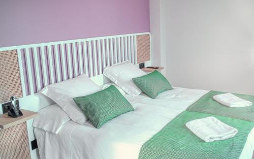 ein weißes Bett mit grünen und weißen Kissen darauf in der Unterkunft HOTEL PORTOMARÍN STAR in Portomarin