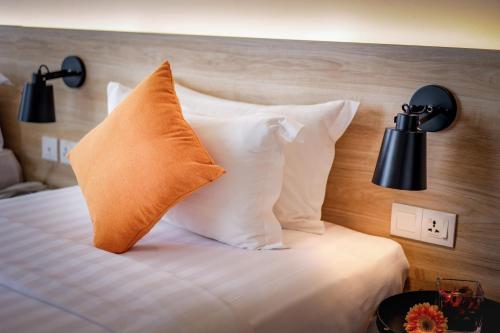 a bed with white pillows and an orange pillow at Santa Grand Classic Kuala Lumpur, Chinatown in Kuala Lumpur