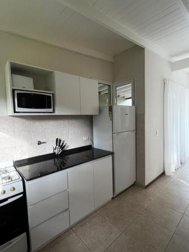 Una cocina con gabinetes blancos, estufa y microondas. en Casa Juno Pinamar Norte, en Pinamar