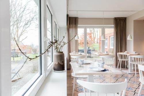 un restaurante con mesas y sillas blancas y ventanas grandes en Aarskogs Boutique Hotel, en Glücksburg