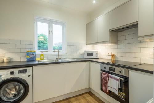 a white kitchen with a washing machine and a sink at Lovely 1 Bed Apartment With FREE PARKING & Garden in Cherry Hinton
