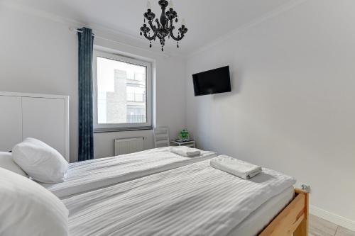 a white bedroom with a large bed with a chandelier at Grobla Centrum 1 by Grand Apartments in Gdańsk