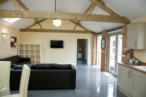 a living room with a black couch and a kitchen at Pheasants Roost at Tove Valley Cottages in Towcester