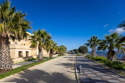 an empty street with palm trees and a building at Fort Chambray Holiday Villas & Apartments in Mġarr